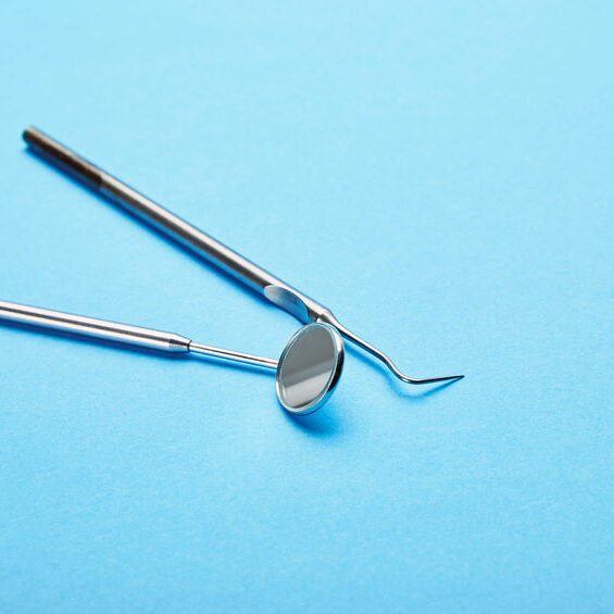 A dental mirror and scaler are placed on a light blue surface.