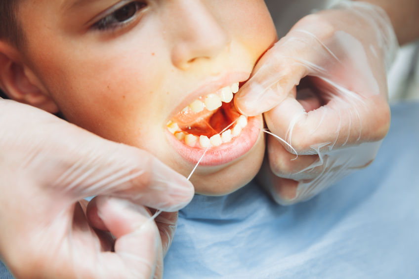 A dentist wearing gloves flosses a young patient's teeth, with a focus on oral hygiene.